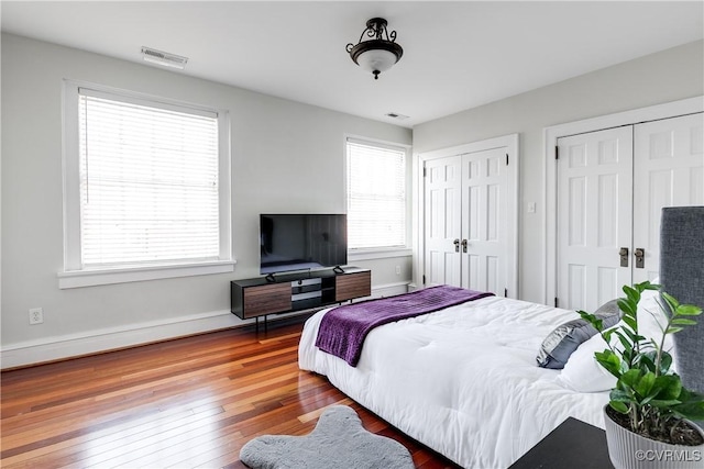 bedroom with wood finished floors, two closets, visible vents, and baseboards