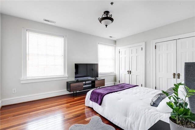 bedroom with wood finished floors, multiple windows, two closets, and visible vents