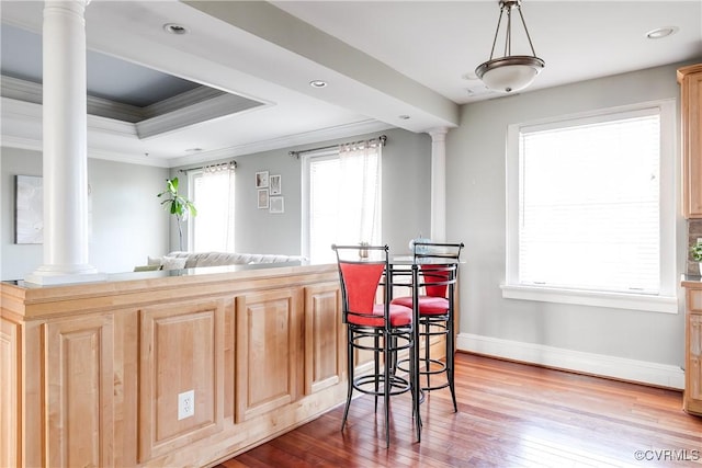 kitchen with hanging light fixtures, ornate columns, a tray ceiling, and wood finished floors