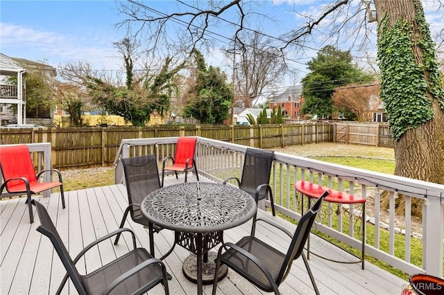 wooden terrace featuring outdoor dining area, a fenced backyard, and a lawn