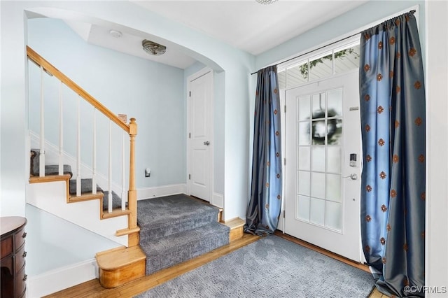 entryway with arched walkways, stairway, wood finished floors, and baseboards