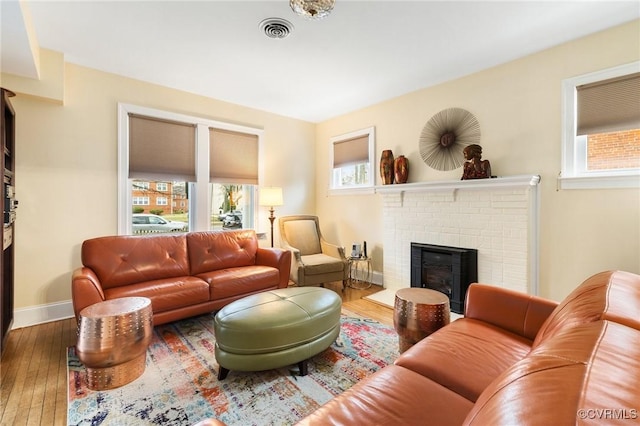 living area featuring baseboards, visible vents, a fireplace, and hardwood / wood-style floors