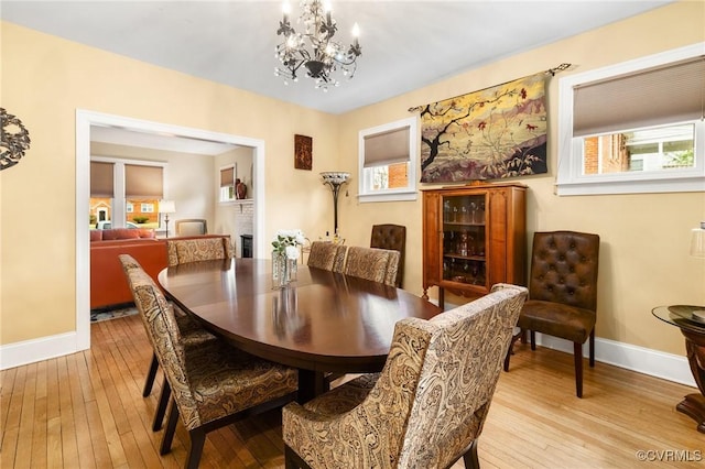 dining space with light wood-type flooring, baseboards, and an inviting chandelier