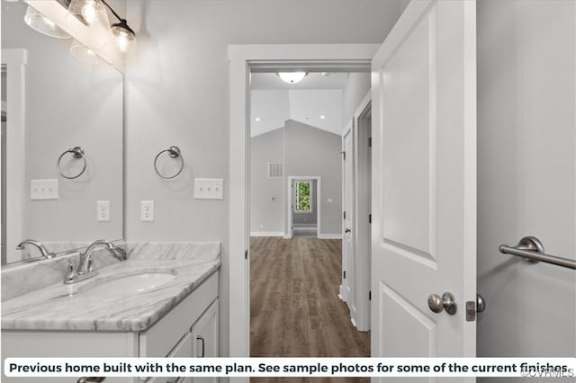 bathroom featuring visible vents, vaulted ceiling, vanity, wood finished floors, and baseboards