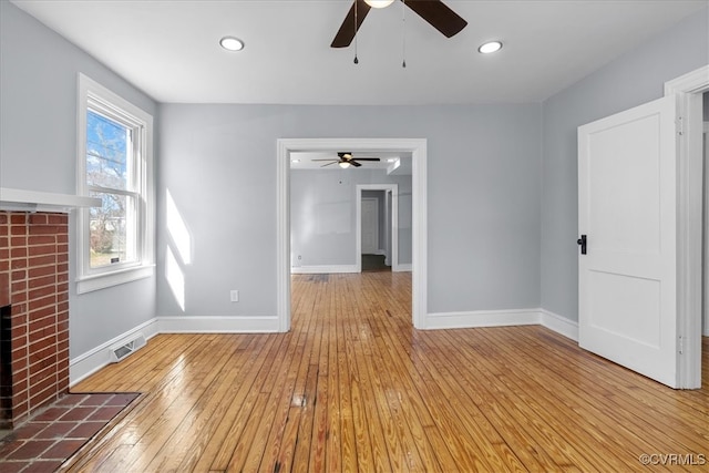 empty room with a brick fireplace, wood-type flooring, visible vents, and baseboards