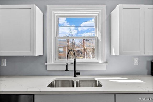 kitchen with dishwasher, a sink, light stone countertops, and white cabinets