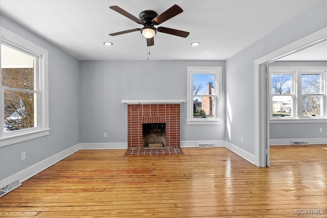 unfurnished living room with light wood-type flooring, a fireplace, visible vents, and a healthy amount of sunlight