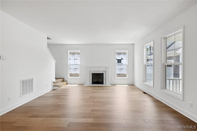 unfurnished living room featuring stairway, visible vents, a wealth of natural light, and light wood-style floors