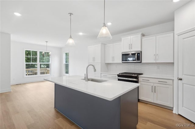 kitchen featuring stainless steel appliances, a sink, white cabinets, light countertops, and an island with sink