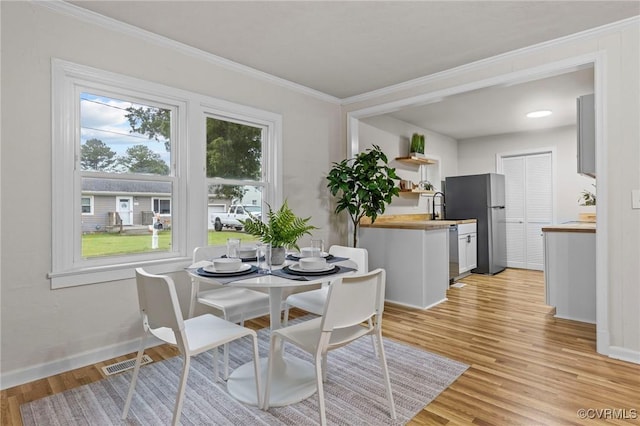 dining space featuring light wood-style floors, baseboards, visible vents, and ornamental molding