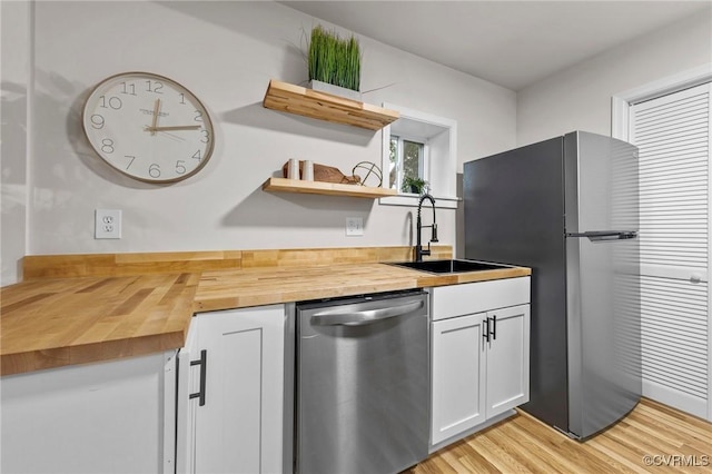 kitchen with butcher block countertops, stainless steel appliances, white cabinetry, open shelves, and a sink