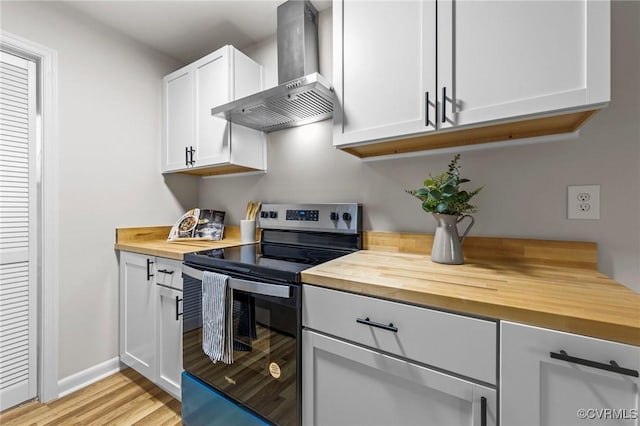 kitchen featuring white cabinets, butcher block counters, wall chimney exhaust hood, light wood-style flooring, and stainless steel electric range