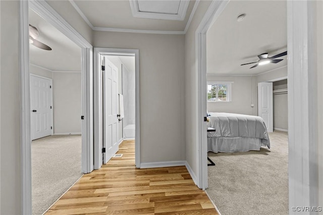 hall with light carpet, ornamental molding, light wood-type flooring, and baseboards