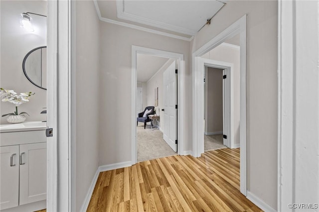 hallway featuring light wood-type flooring, a sink, baseboards, and crown molding