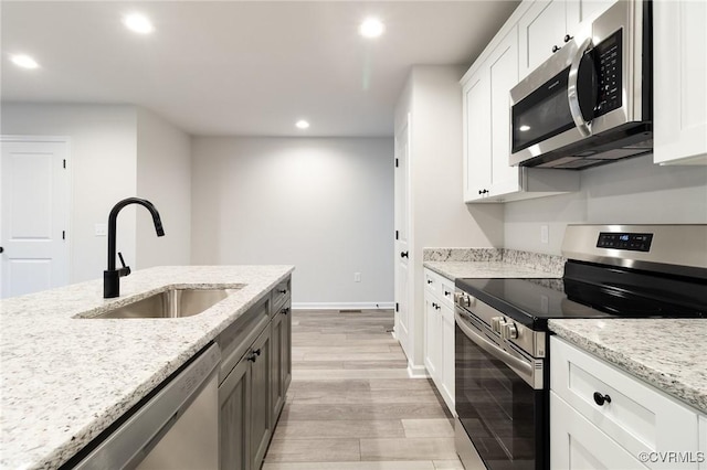 kitchen featuring light stone counters, stainless steel appliances, white cabinetry, a sink, and recessed lighting