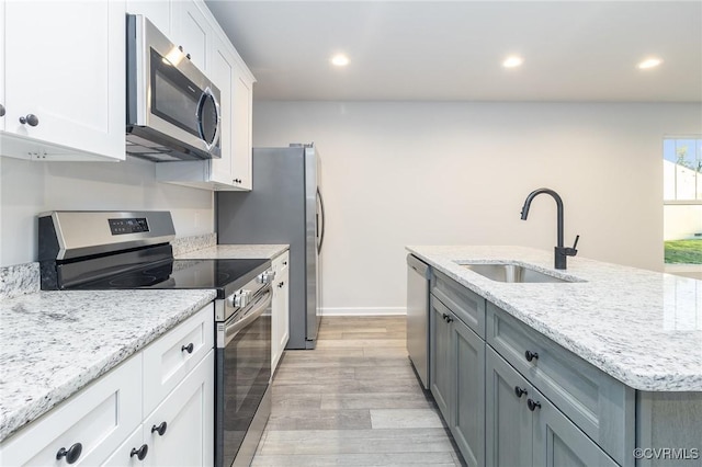 kitchen featuring appliances with stainless steel finishes, light stone counters, a kitchen island with sink, white cabinetry, and a sink