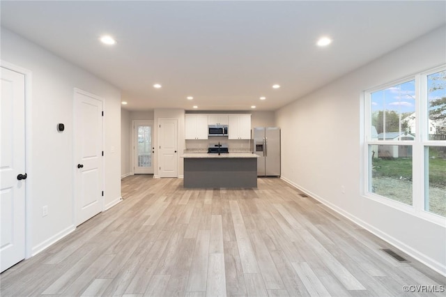 kitchen featuring stainless steel appliances, light countertops, visible vents, white cabinets, and an island with sink