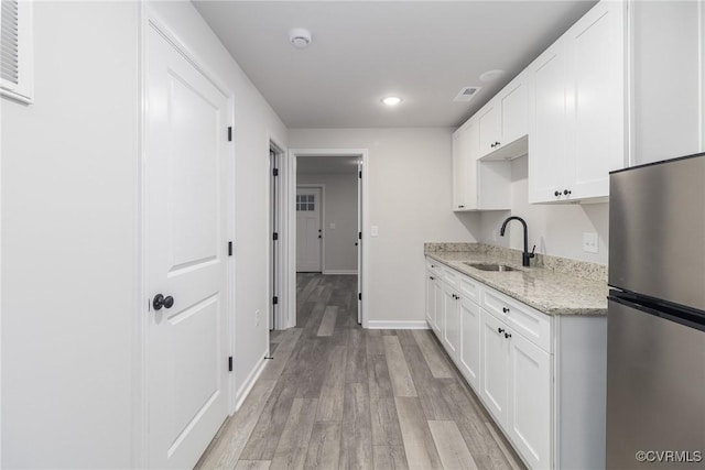 kitchen with light stone counters, white cabinets, a sink, and freestanding refrigerator