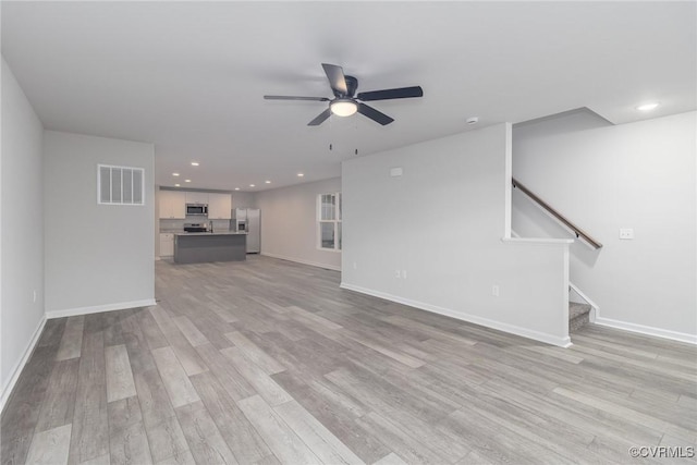 unfurnished living room featuring light wood-type flooring, visible vents, ceiling fan, and stairway