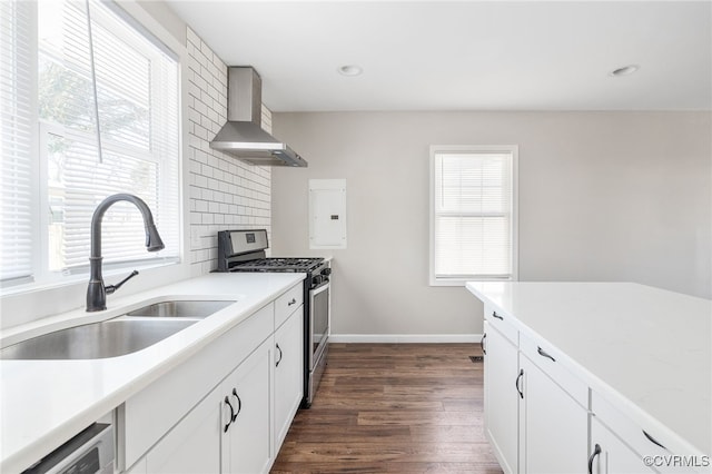 kitchen featuring wall chimney exhaust hood, light countertops, white cabinetry, a sink, and gas stove