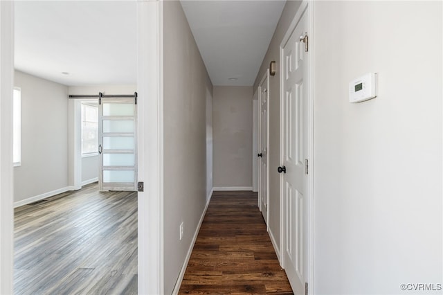 corridor with dark wood-style floors, a barn door, and baseboards