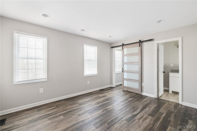 unfurnished bedroom featuring a barn door, dark wood finished floors, visible vents, and baseboards