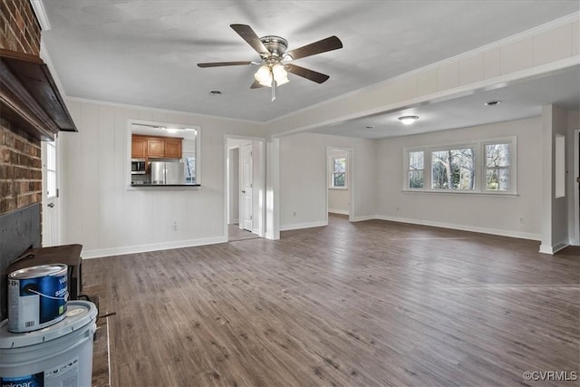 unfurnished living room with baseboards, ornamental molding, ceiling fan, and dark wood-type flooring