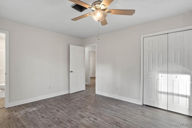 unfurnished bedroom with dark wood-style floors, a closet, ensuite bathroom, and baseboards