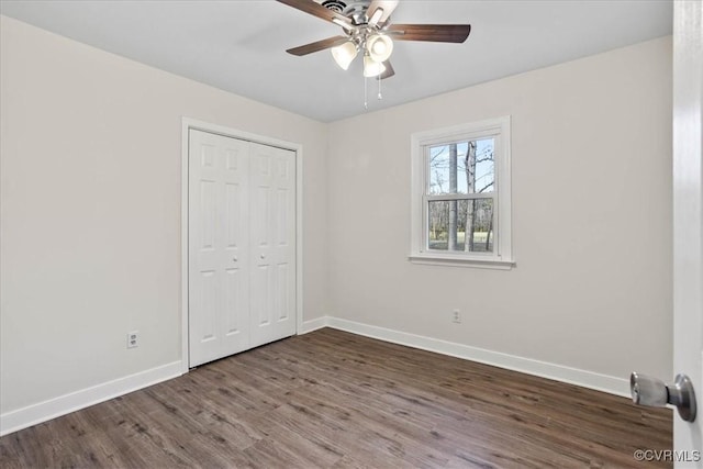 unfurnished bedroom featuring dark wood-type flooring, a closet, baseboards, and a ceiling fan