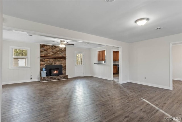 unfurnished living room with dark wood-type flooring, a brick fireplace, a ceiling fan, and baseboards