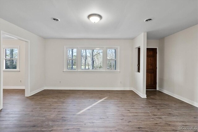 empty room with dark wood-type flooring, a healthy amount of sunlight, and visible vents