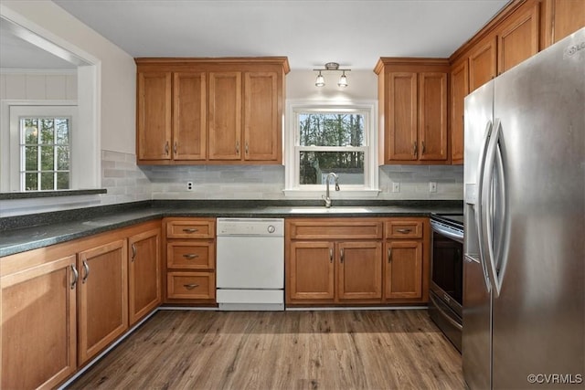 kitchen featuring appliances with stainless steel finishes, brown cabinetry, a sink, and wood finished floors