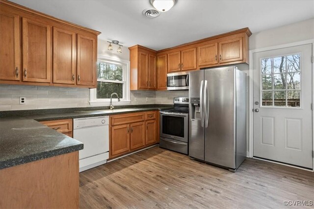 kitchen with visible vents, brown cabinetry, stainless steel appliances, light wood-type flooring, and a sink