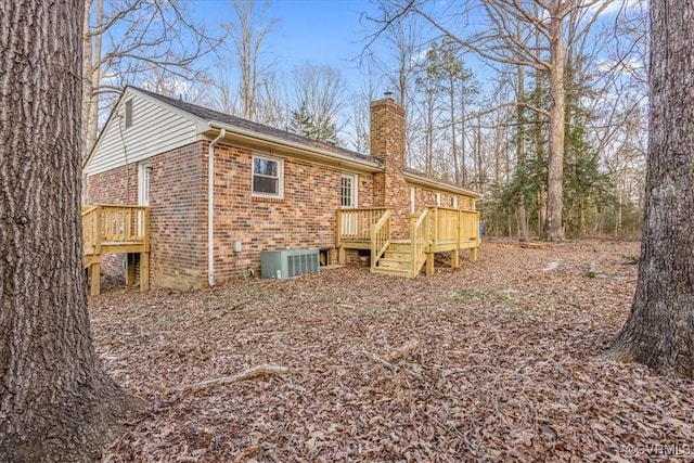 rear view of house featuring a deck, central AC, brick siding, and a chimney