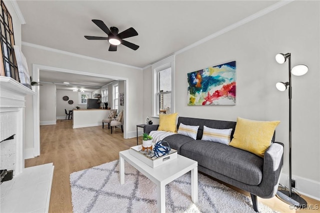 living room featuring light wood-style flooring, baseboards, a fireplace with raised hearth, and crown molding