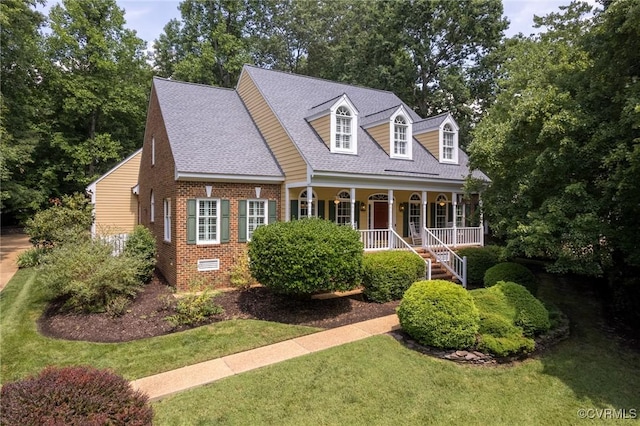 new england style home featuring brick siding, roof with shingles, a porch, a front yard, and crawl space