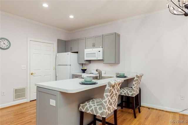 kitchen featuring a breakfast bar, white appliances, light countertops, and a peninsula