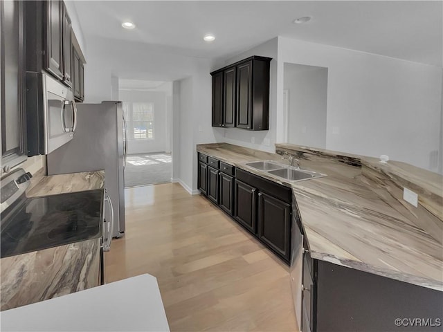 kitchen with wooden counters, appliances with stainless steel finishes, a sink, dark cabinets, and light wood-type flooring