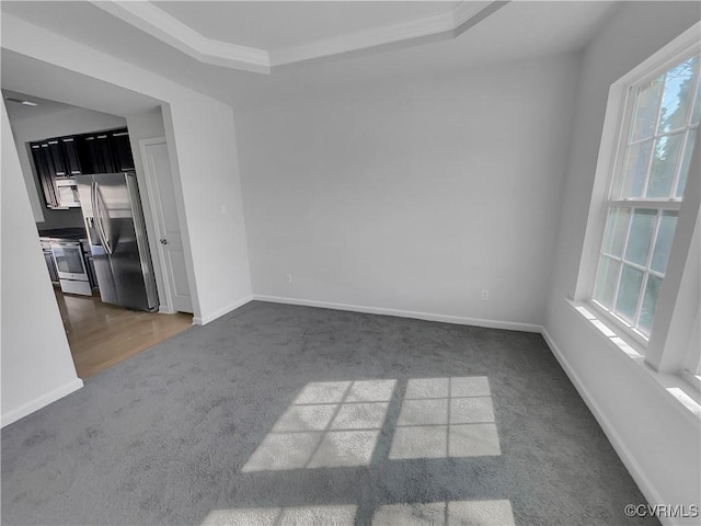 spare room featuring baseboards, dark carpet, a raised ceiling, and crown molding