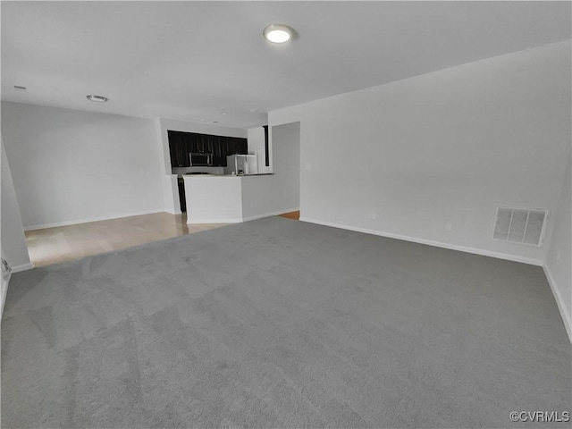 unfurnished living room with dark carpet, visible vents, and baseboards