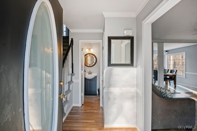 hall with wood finished floors, a sink, baseboards, stairway, and crown molding