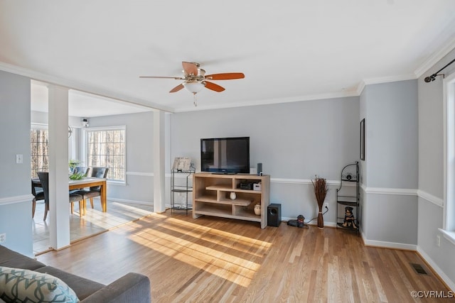 living room with crown molding, light wood finished floors, visible vents, and baseboards