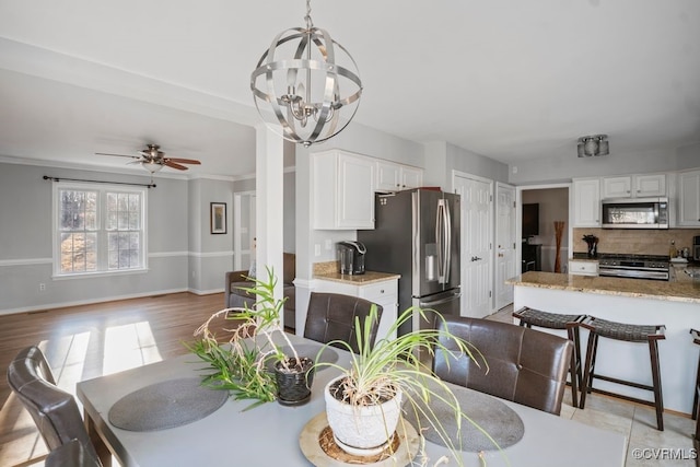 dining area with light wood-style floors, baseboards, crown molding, and ceiling fan with notable chandelier