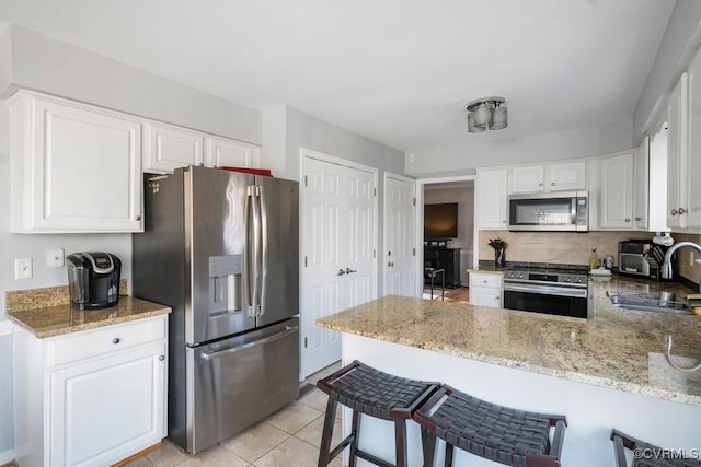 kitchen with a peninsula, light stone counters, stainless steel appliances, and a sink