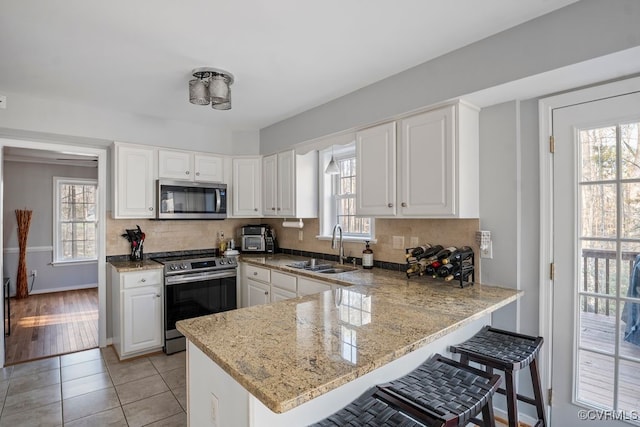 kitchen with a peninsula, a sink, white cabinets, appliances with stainless steel finishes, and tasteful backsplash