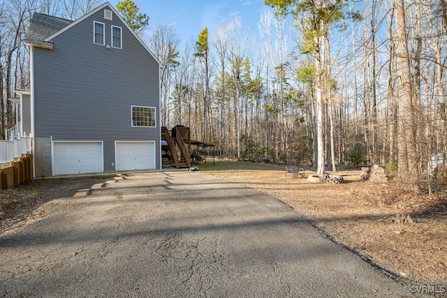 view of side of property featuring driveway, an attached garage, stairway, and a shingled roof