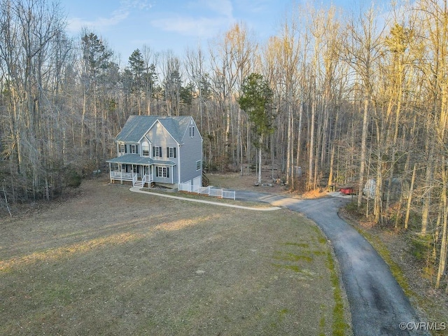 view of front of property with driveway, a front yard, and a view of trees