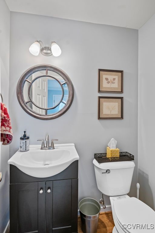 half bathroom featuring toilet, wood finished floors, and vanity