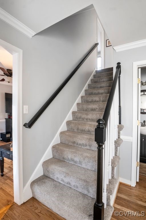 stairway featuring a ceiling fan, baseboards, ornamental molding, and wood finished floors