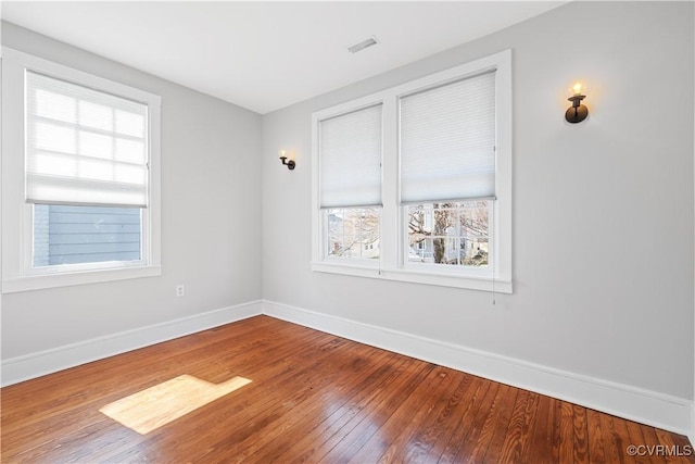 unfurnished room featuring visible vents, hardwood / wood-style floors, and baseboards